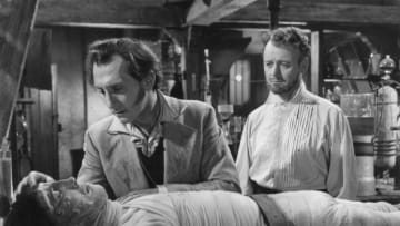 1957: Baron Frankenstein, played by Peter Cushing (1913 - 1994), leans over the monster he has created, Christopher Lee, as Robert Urquhart (1921 - 1995) looks on. The scene is from 'The Curse of Frankenstein', directed by Terence Fisher. (Photo by Hulton Archive/Getty Images)