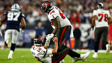 TAMPA, FL - JANUARY 16: Shaq Mason #69 of the Tampa Bay Buccaneers helps Tom Brady #12 off the ground after a play during the fourth quarter of an NFL wild card playoff football game against the Dallas Cowboys at Raymond James Stadium on January 16, 2023 in Tampa, Florida. (Photo by Kevin Sabitus/Getty Images)