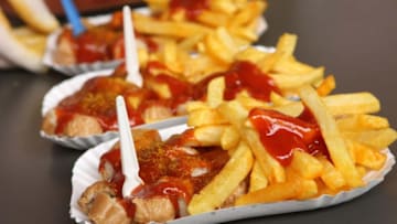 BERLIN, GERMANY - JULY 14: An employee prepares plates of currywurst with french fries at Konnopke's currywurst stand on July 14, 2012 in Berlin, Germany. Currywurst, originally founded in post-war Berlin by Herta Heuwa, is Berlin's answer to fast food and is sold at specialized stands across the city and the rest of Germany. Currywurst is pork sausage, with or without casing, fried or deep-fried, that is typically smothered in curry powder and a ketchup-like sauce called curry sauce and served with french fries. (Photo by Adam Berry/Getty Images)