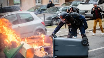 PARIS, FRANCE - FEBRUARY 22: A police officer handles a burning rubbish bin after clashes between police and rioters took place while High school students gather for a demonstration to support Theo and against Police violence at Place de la Nation on February 23, 2017 in Paris, France. Theo, 22, was arrested by four policemen in the Rose des Vents district of Aulnay sous Bois in Seine Saint Denis on Thursday, February 2nd. He was later admitted to hospital, suffering serious injuries after allegedly been sodomized by police officers with a truncheon. The scene was filmed and widely distributed, before one of the policemen was charged with rape, the other three for voluntary violence, all officers have been suspended. (Photo by Aurelien Morissard/IP3/Getty Images)