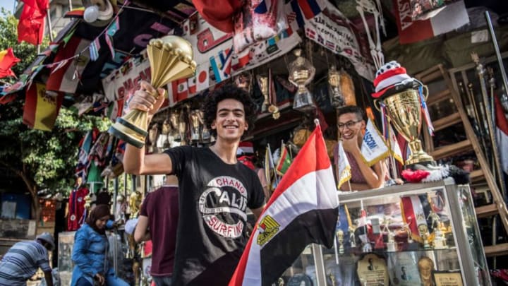 An Egyptian youth holds a replica model of the Afican Cup of Nations trophy in one hand an a national flag in the other as he stands outside a shop selling trophies and medals and other sports memorabilia in the capital Cairo's downtown district on June 17, 2019. (Photo by Khaled DESOUKI / AFP) (Photo credit should read KHALED DESOUKI/AFP/Getty Images)