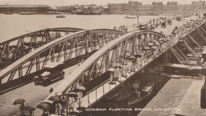 Howrah Floating Bridge, Calcutta', 1905. Howrah Bridge, a pontoon bridge over the Hooghly River in West Bengal, India. The Government of Bengal passed the Howrah Bridge Act in the year 1871 under the Bengal Act IX of 1871. A contract was signed with Bradford Leslie (1831-1926) to construct a pontoon bridge. Parts of the bridge were constructed in England and shipped to Calcutta, where they were assembled. The bridge was completed in 1874. [The Commercial Union, Calcutta, circa 1905]. Artist: Unknown. (Photo by The Print Collector/Getty Images)
