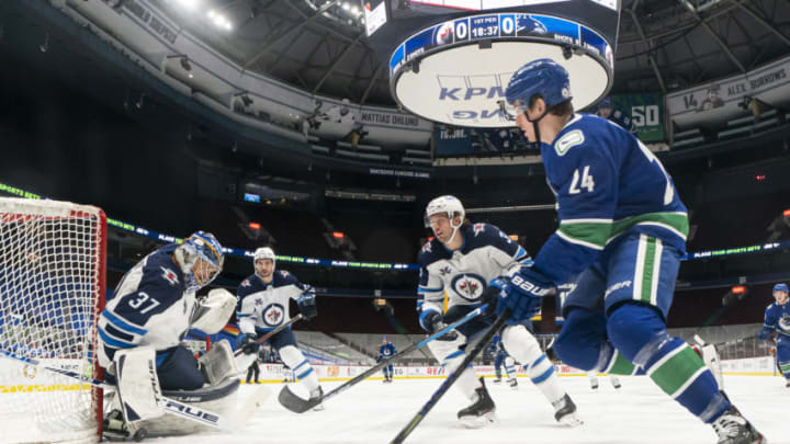 VANCOUVER, BC - MARCH 22: Goalie Connor Hellebuyck #37 and Tucker Poolman #3 of the Winnipeg Jets defends Jimmy Vesey #24 of the Vancouver Canucks during the first period of NHL action at Rogers Arena on March 22, 2021 in Vancouver, Canada. (Photo by Rich Lam/Getty Images)