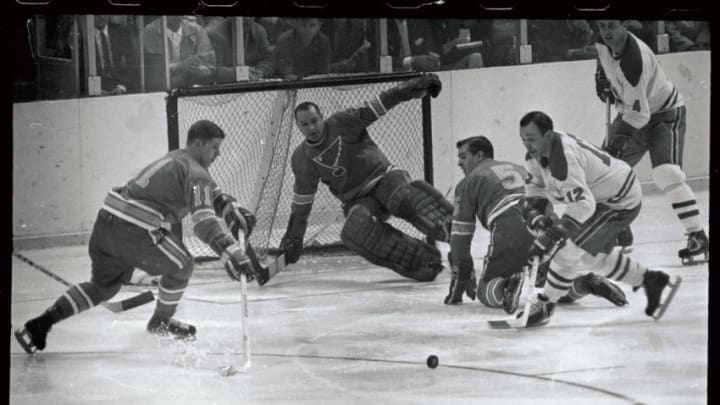 (Original Caption) St. Louis Blue's Bob Plager (5) hits the ice as goalie Glenn Hall blocks a shot by Montreal's Yvan Cournoyer (12) and pushes the puck in front of the goal where Cournoyer and Blues Gary Sabourini (11) battle for control of the puck. The action was in the 1st period of Blues-Canadians game here. Canadian's Jean Beliveau (4) watches the action.