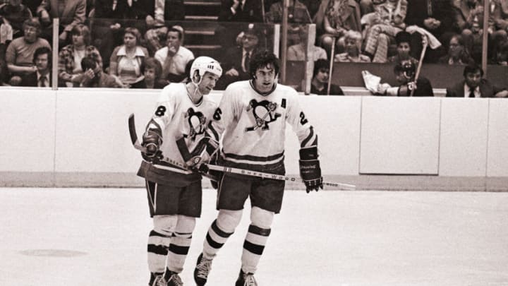 PITTSBURGH, PA - CIRCA 1976: (EDITORS NOTE: Image has been shot in black and white. Color version not available.) Winger Lowell MacDonald #18 and center Syl Apps, Jr. #26 of the Pittsburgh Penguins look on from the ice during a timeout during a National Hockey League game at the Civic Arena circa 1976 in Pittsburgh, Pennsylvania. (Photo by George Gojkovich/Getty Images)