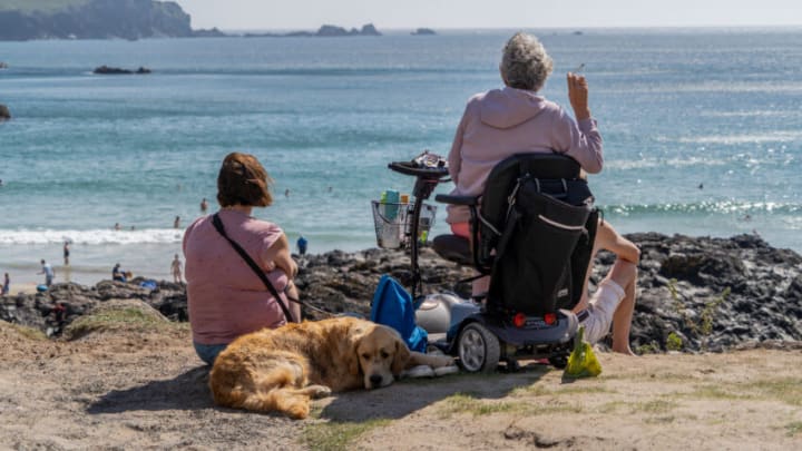CORNWALL, UNITED KINGDOM - 2021/09/11: Elderly lady enjoys a cigarette looking at the coastline at Kynance Cove in Cornwall.Kynance Cove is a favourite holiday destination in Cornwall. The Cove boasts clear blue waters and soft white sand. Each year tens of thousands come to this remote part of Cornwall just to see Kynance Cove and swim in its blue waters. (Photo by Edward Crawford/SOPA Images/LightRocket via Getty Images)