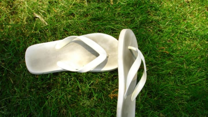 A pair of really dirty white flip-flops sitting on top of very green grass