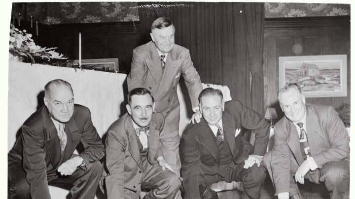 (Original Caption) Famed Coach Bob zuppke of the University of Illinois returned to the campus here Thursday night (10/27) to be feted at a banquet. He is shown standing behind the backfield of his 1924 team. The men are (left to right) Harry Hall, who was quarterback; Wally McLwain, right half; Earl Britton, full; and Red Grange, left half..