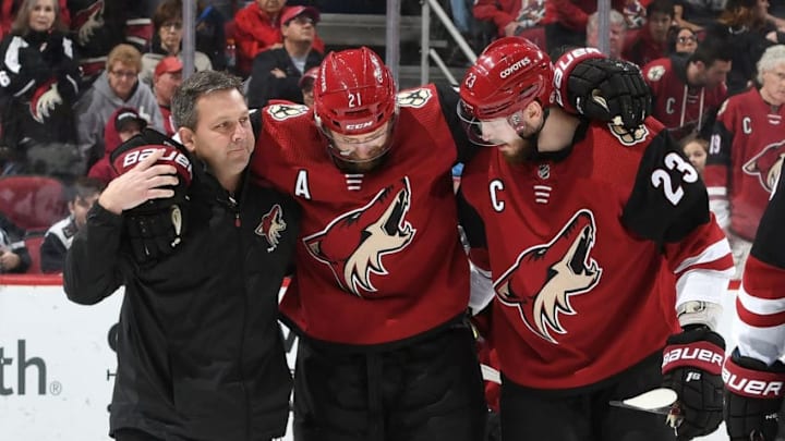 GLENDALE, AZ - FEBRUARY 28: Derek Stepan #21 of the Arizona Coyotes is helped off the ice by teammate Oliver Ekman-Larsson #23 and team trainer Dave Zenobi after Stepan suffered an injury against the Vancouver Canucks during the third period at Gila River Arena on February 28, 2019 in Glendale, Arizona. (Photo by Norm Hall/NHLI via Getty Images)