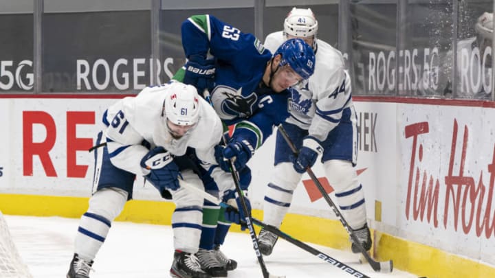 VANCOUVER, BC - MARCH 04: Bo Horvat #53 of the Vancouver Canucks battles with Nic Petan #61 and Morgan Rielly #44 of the Toronto Maple Leafs for the puck during NHL hockey action at Rogers Arena on March 4, 2021 in Vancouver, Canada. (Photo by Rich Lam/Getty Images)