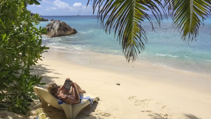 LA PASSE, LA DIGUE, SEYCHELLES - OCTOBER 03, 2015: Woman is reading in a Amazon Kindle ebook reader under palmtrees at Patata beach on October 03, 2015 in La Passe, La Digue, Seychelles. (Photo by EyesWideOpen/Getty Images)