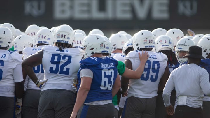 The word ‘believe’ is seen in the background as Kansas players huddle up at the beginning of Tuesday’s outdoor practice.
