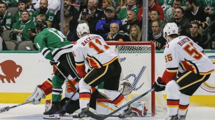 DALLAS, TX - DECEMBER 18: Dallas Stars left wing Jamie Benn (14) scores against Calgary Flames goaltender David Rittich (33) as center Mikael Backlund (11) tries to defend during the game between the Dallas Stars and the Calgary Flames on December 18. 2018 at the American Airlines Center in Dallas Texas.(Photo by Matthew Pearce/Icon Sportswire via Getty Images)