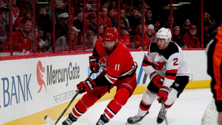RALEIGH, NC - MARCH 2: Jordan Staal #11 of the Carolina Hurricanes plays a loose puck behind the net and controls it away from John Moore #2 of the New Jersey Devils during an NHL game on March 2, 2018 at PNC Arena in Raleigh, North Carolina. (Photo by Gregg Forwerck/NHLI via Getty Images)