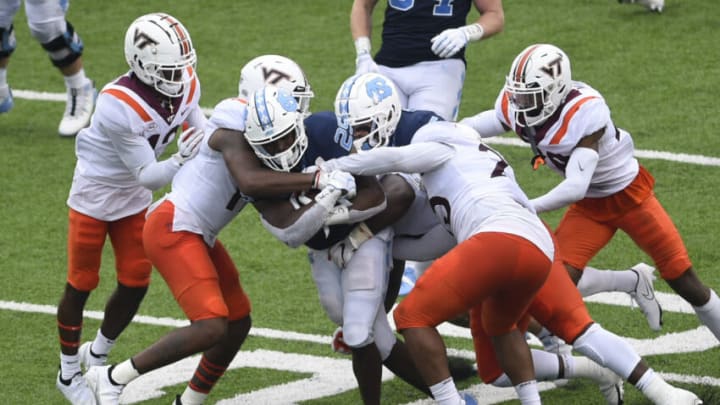 Oct 10, 2020; Chapel Hill, North Carolina, USA; North Carolina Tar Heels running back Javonte Williams (25) with the ball as Virginia Tech Hokies defensive backs Nadir Thompson (12) and J.R. Walker (19) and linebacker Rayshard Ashby (23) and defensive lineman Norell Pollard (96) and defensive back Jermaine Waller (28) defend in the third quarter at Kenan Memorial Stadium. Mandatory Credit: Bob Donnan-USA TODAY Sports