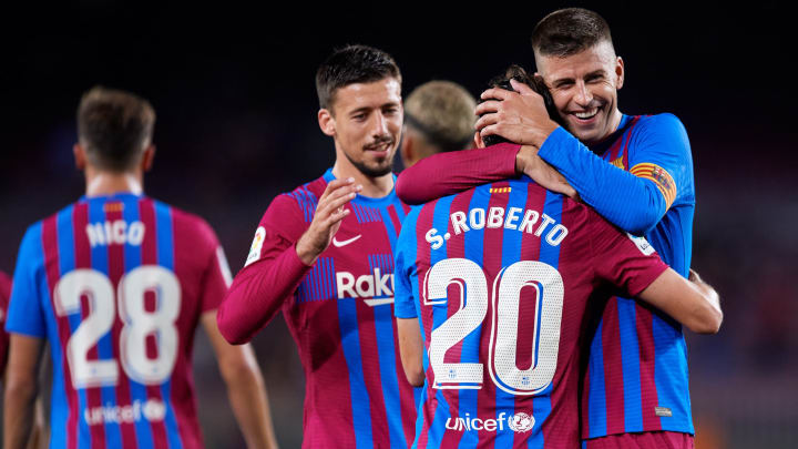 BARCELONA, SPAIN – AUGUST 15: Sergi Roberto of FC Barcelona celebrates with his teammates Gerard Pique and Clement Lenglet after scoring their team’s fourth goal during the LaLiga Santander match between FC Barcelona and Real Sociedad at Camp Nou on August 15, 2021 in Barcelona, Spain. FC Barcelona will host between 20,000 and 22,000 fans in the stadium as the Regional government has authorised a capacity of 30 percent of the stadium with the requirement to maintain a meter and a half distance between people or groups of people who have tickets. (Photo by Alex Caparros/Getty Images)