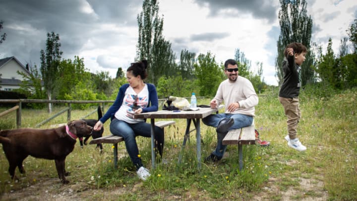LAS MATAS, MADRID, SPAIN - MAY 13: Carolina resting with her husband Alfonso on a park picnic table feeds her dog, Shiva, as their kid Pablito plays jumping from the bench to the floor on May 13, 2020 in Las Matas, Madrid, Spain. As Spain eases its coronavirus lockdown measures, Carolina, who is five months pregnant, is still staying close to home as a precaution. She spends most of her time with her family or studying online to become a primary school teacher. The only exceptions to her home confinement are when she goes for a walk, to the supermarket, or for medical checkups. (Photo by Pablo Cuadra/Getty Image)