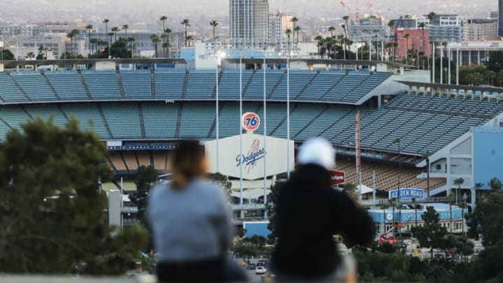 LOS ANGELES, CALIFORNIA - MARCH 26: People sit on a hill overlooking Dodger Stadium on what was supposed to be Major League Baseball's opening day, now postponed due to the coronavirus, on March 26, 2020 in Los Angeles, California. The Los Angeles Dodgers were slated to play against the San Francisco Giants at the stadium today. Major League Baseball Commissioner Rob Manfred recently said the league is "probably not gonna be able to" play a full 162 game regular season due to the spread of COVID-19. (Photo by Mario Tama/Getty Images)