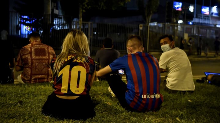 A couple wearing Lionel Messi jerseys sit in the grass as supporters gather in front of the Camp Nou stadium in Barcelona on August 5, 2021. (Photo by PAU BARRENA/AFP via Getty Images)