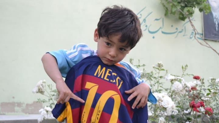QUETTA, PAKISTAN - MAY 03: Murtaza Ahmedi, a five year old Afghan boy who wears a jersey signed by Messi, poses as he holds another jersey from Messi in Quetta of Balochistan province, a South-Western city in Pakistan on May 3, 2016. A boy from Ghazni province of Afghanistan became famous on social media in the world after wearing a plastic bag shirt resembling the uniform of international football star Lionel Messi. Messi had also expressed his wish to meet Murtaza Ahmedi. Parents of Murtaza Ahmedi moved him to Quetta from Afghanistan hence they worried about kidnapping, Mr. Wahid Ahmedi, a relative of the boy said. They also appealed to football federations and both Afghanistan and Pakistan government for making arrangements of meeting between Lionel Messi and Murtaza Ahmedi. (Photo by Mazhar Chandio/Anadolu Agency/Getty Images)