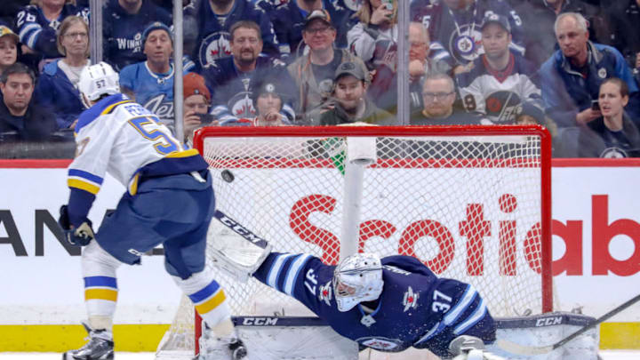 WINNIPEG, MB - DECEMBER 27: David Perron #57 of the St. Louis Blues shoots the puck over a sprawled Connor Hellebuyck #37 of the Winnipeg Jets for the overtime winning goal at the Bell MTS Place on December 27, 2019 in Winnipeg, Manitoba, Canada. (Photo by Darcy Finley/NHLI via Getty Images)