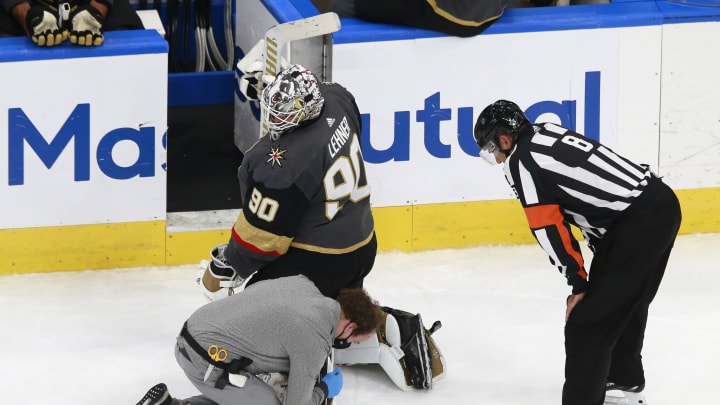 An equipment manager works on the broken skate of Robin Lehner #90 of the Vegas Golden Knights as referee Dave Jackson #8 looks on against the Chicago Blackhawks during the second period in Game One of the Western Conference First Round.