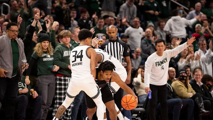 Dec 21, 2021; Detroit, Michigan, USA; Michigan State Spartans guard A.J. Hoggard (11) dribbles away from Oakland Golden Grizzlies guard Jalen Moore (34) and forward Micah Parrish (3) during the final seconds of the second half at Little Caesars Arena. Mandatory Credit: Raj Mehta-USA TODAY Sports