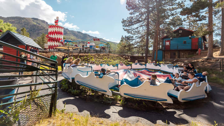 Young riders enjoy the Mini-Himalaya ride, with the Peppermint Slide and Tilt-A-Whirl in the forested background of North Pole, Colorado. Photo courtesy North Pole / design rangers.