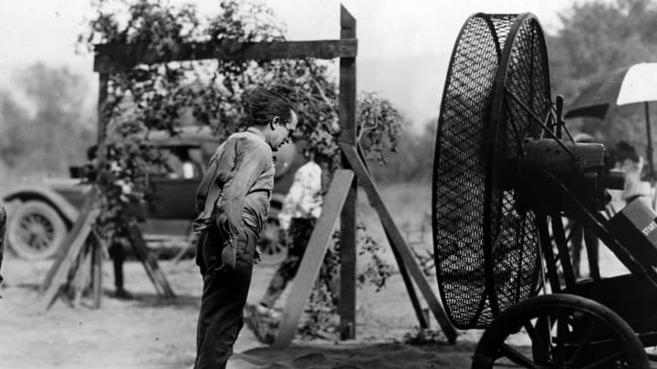 circa 1925: Harold Lloyd (1893 – 1971), the American film comedian puts a wind machine to good use to blow himself clean after rolling in the dust during a film sequence.  Hey, it’s a big fan… generates a… draft.  Get it?  (Photo by Hulton Archive/Getty Images)