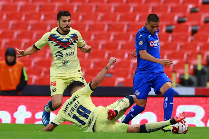Jugadores de América pelean un balón ante un elemento de Cruz Azul.