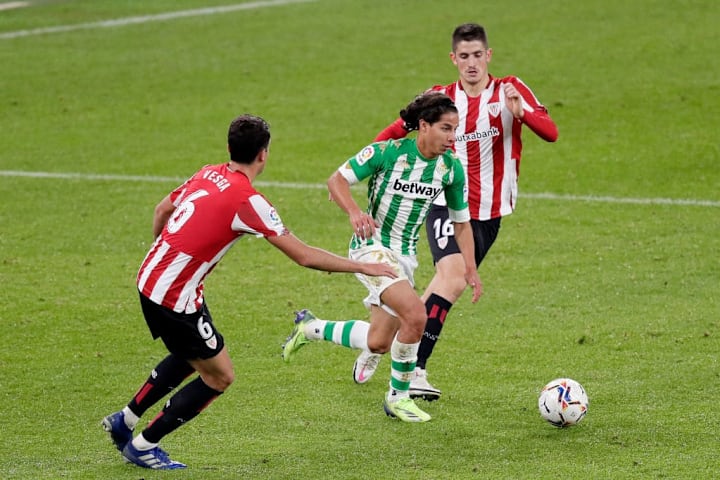 Diego Lainez sale con el balón entre dos rivales.