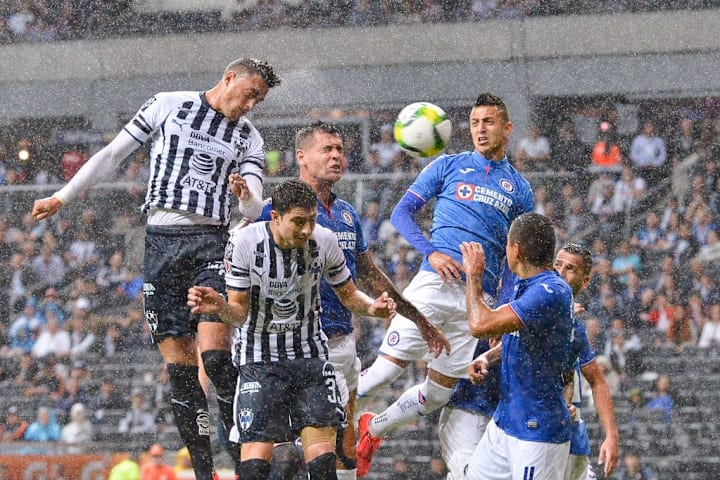 Jugadores de Rayados de Monterrey y Cruz Azul pelean una pelota por los aires.