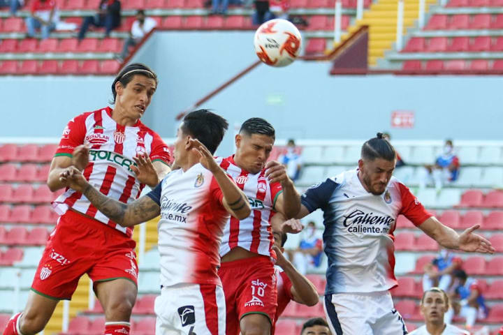 Jugadores de Necaxa y Chivas pelean un balón por lo alto.