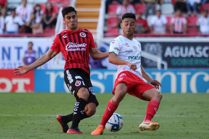 Jugadores de Xolos de Tijuana y de Necaxa pelean un balón.