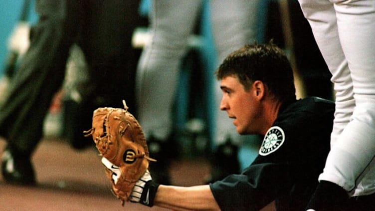 SEATTLE, UNITED STATES: Amidst a sea of his teammates' legs, Seattle Mariner catcher Dan Wilson displays the Barry Bonds foul ball he caught while sliding onto the step of the Seattle dugout during third inning play against the San Francisco Giants in Seattle WA, 11 June 1999. Seattle went on to win, 7-3. AFP PHOTO Dan Levine (Photo credit should read DAN LEVINE/AFP via Getty Images)