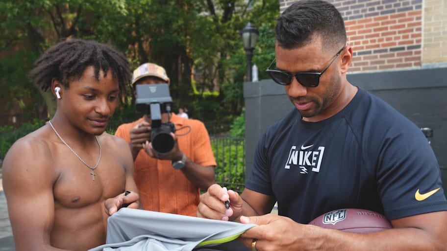 Russell Wilson signs an autograph for a fan who has just taken off his shirt to hand it to him.