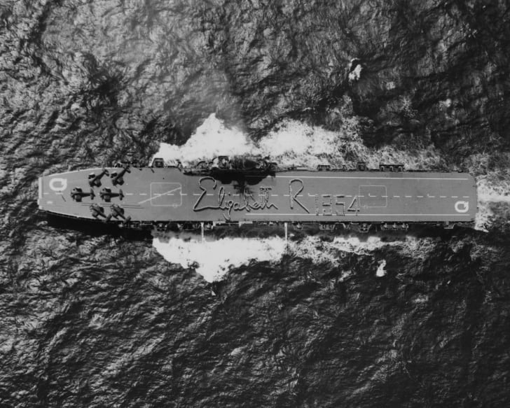 O HMAS Vengeance visto de um helicóptero, enquanto a tripulação da Naval australiana soletrava a assinatura da Rainha Elizabeth II no convés, em 1954.