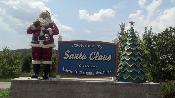 A statue of Santa Claus stands above a ‘Welcome to Santa Claus, Indiana’ sign.
