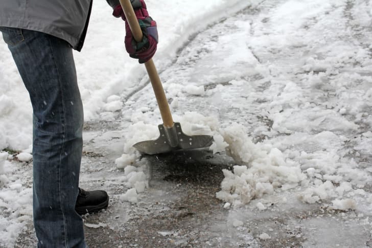 A man shoveling slushy snow in a driveway.