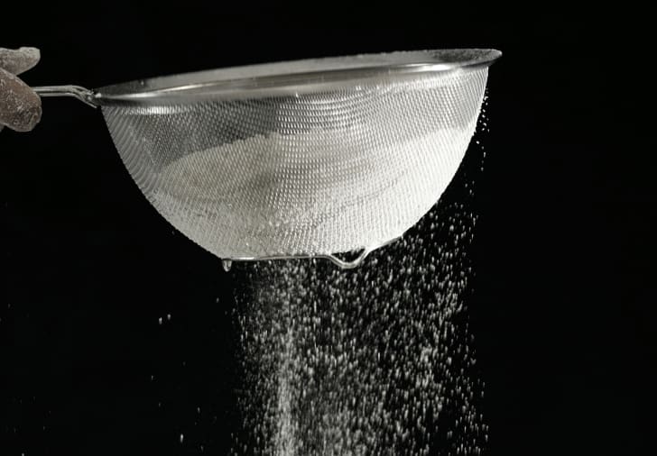 Flour being sifted in front of a black background.
