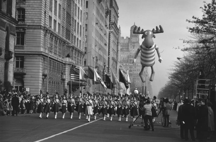 A black and white picture of an early Macy's Thanksgiving Day Parade, with a marching band in the foreground and an inflatable balloon of Bullwinkle the moose in the background.