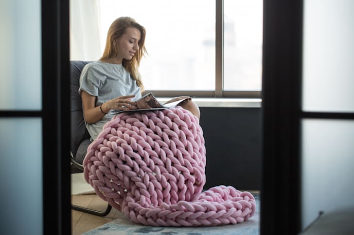 Woman reading with a knit blanket on her lap.