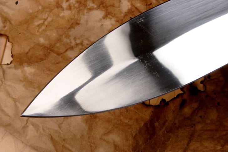 A steel sword point over a background of burned paper