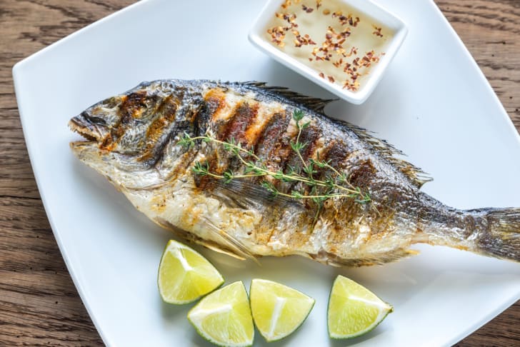 A whole grilled fish on a plate with lemons.