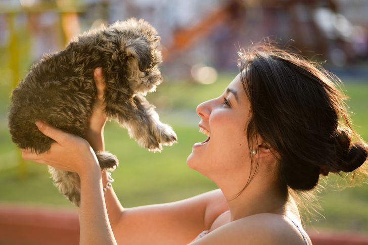 A woman holds up a puppy.