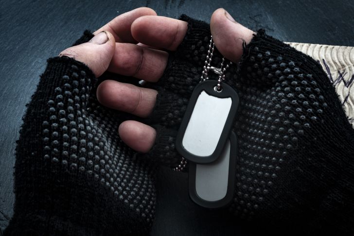 Hands with fingerless gloves holding military tags.