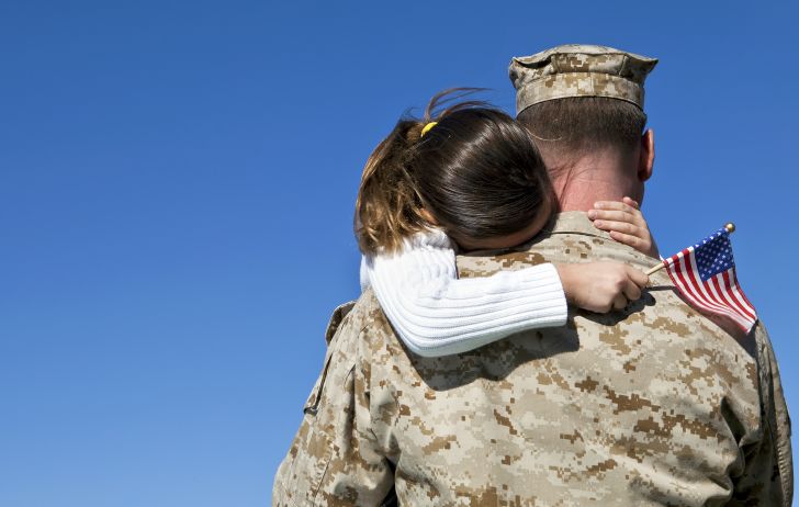 Young girl holding American flag embracing man in military uniform.
