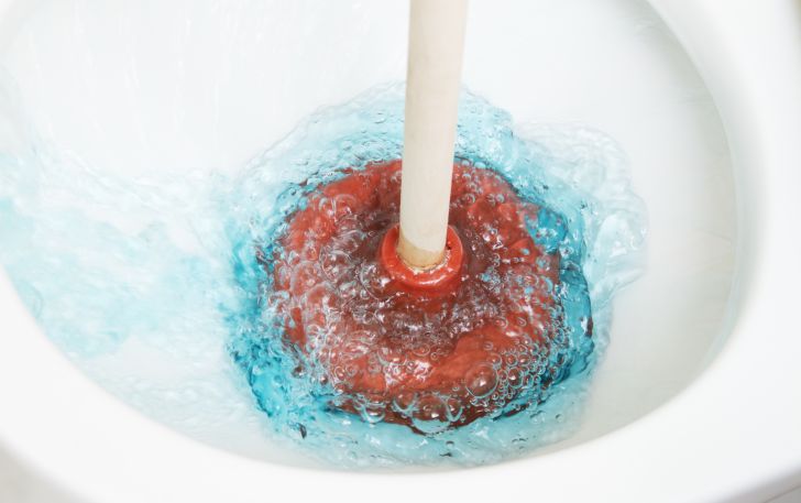 Using a plunger on a backed-up toilet.