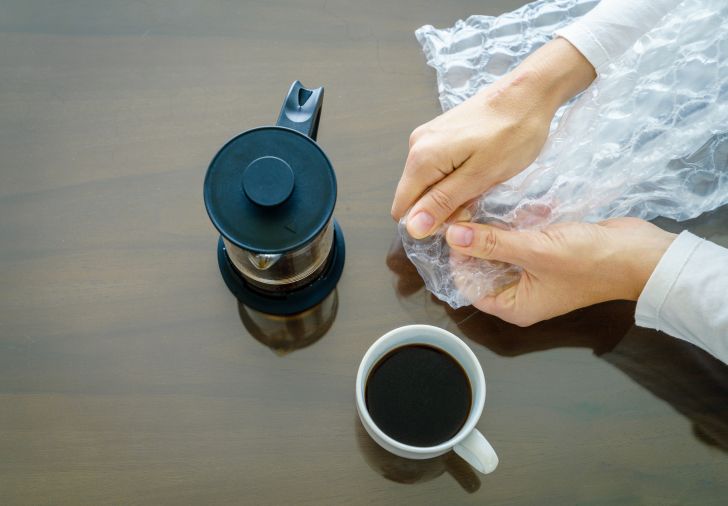 Woman popping Bubble Wrap on a table with coffee nearby.