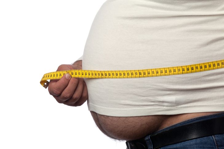 Up-close shot of an overweight man measuring his belly.